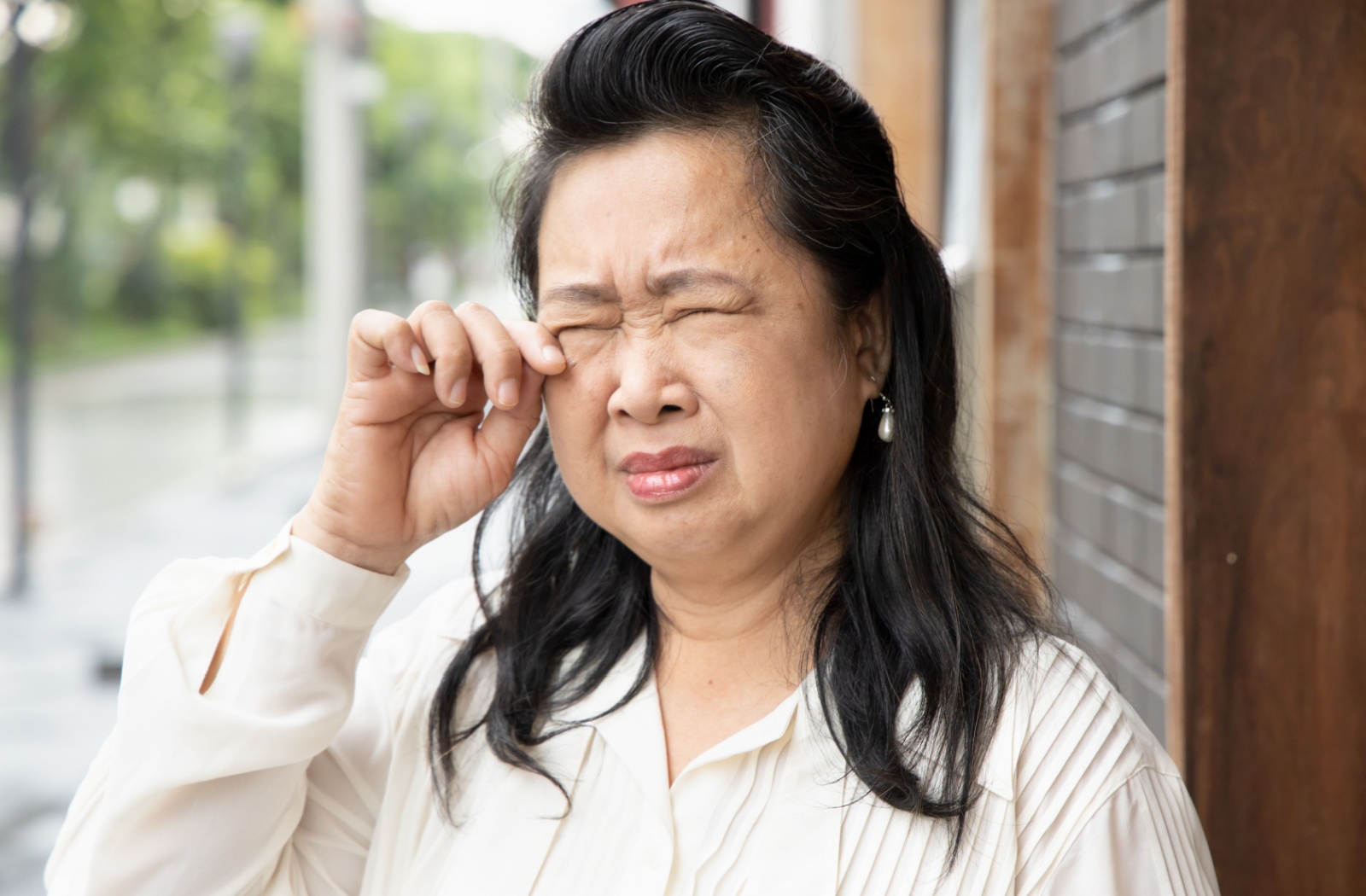 A person squinting while they rub their irritated eyes caused by dry eye