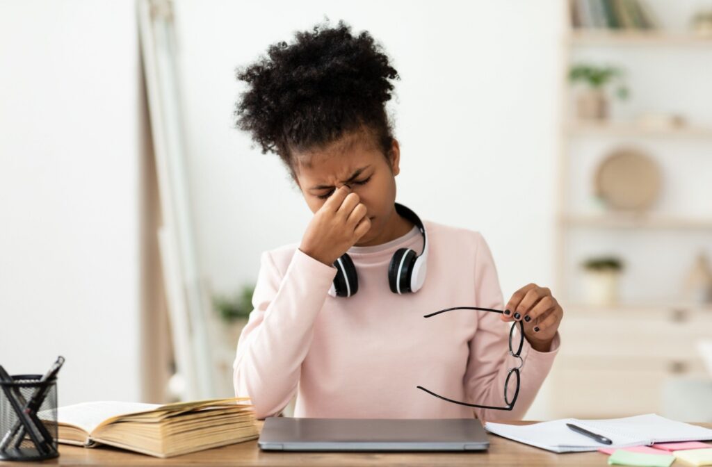 A person rubbing their irritated eyes after removing their glasses