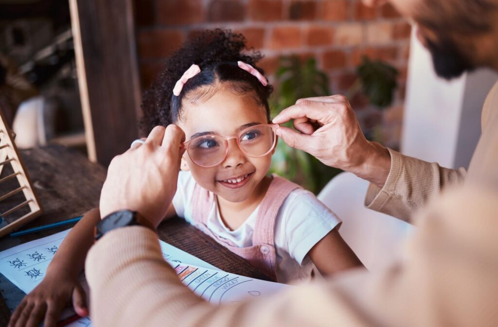 A parent putting a pair of pink glasses on their child as the child smiles