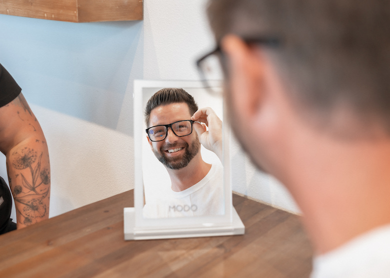 male patient inspecting new eyeglass frames in a mirror